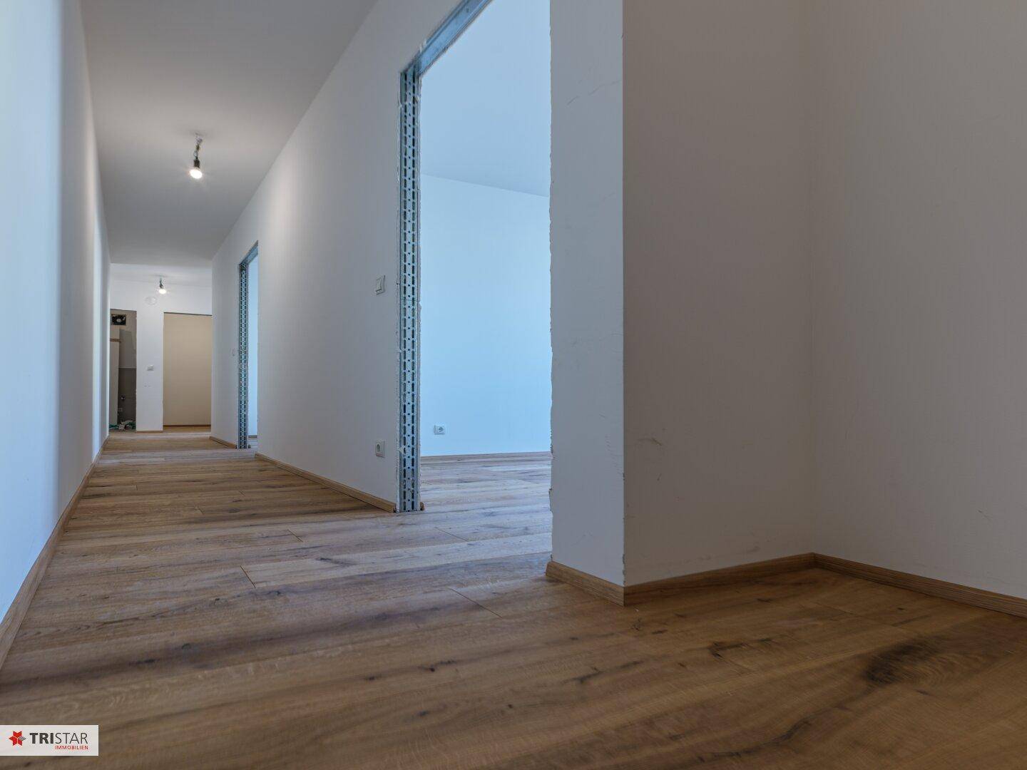 Langer, heller Flur mit Holzboden und weißen Wänden, der zu weiteren Räumen führt.