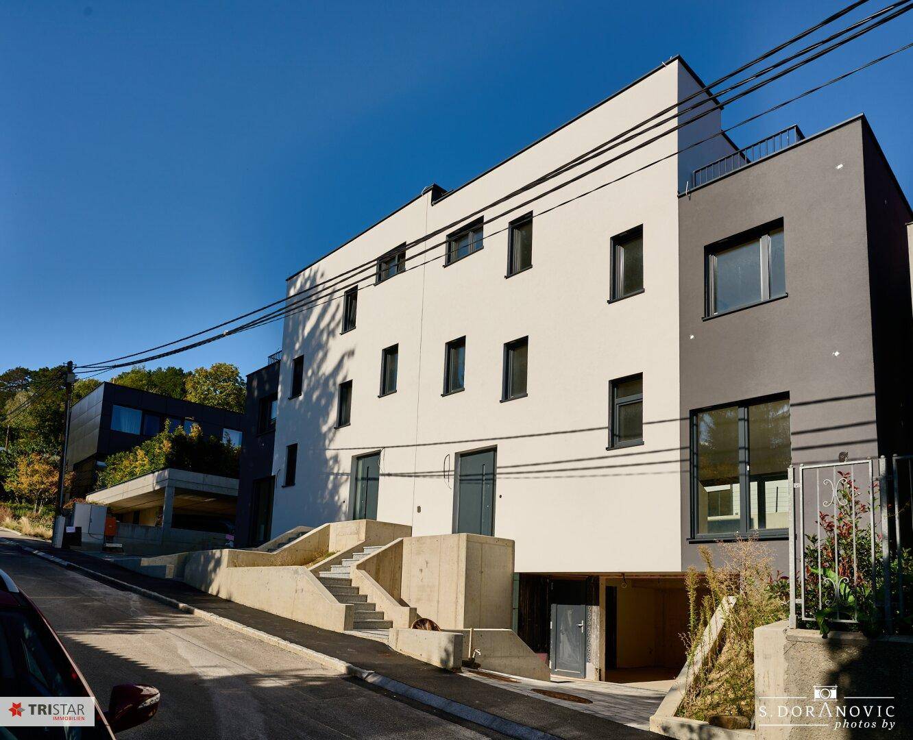 Moderne Fassade eines Neubaus mit weißem und grauem Putz sowie mehreren Fenstern.
