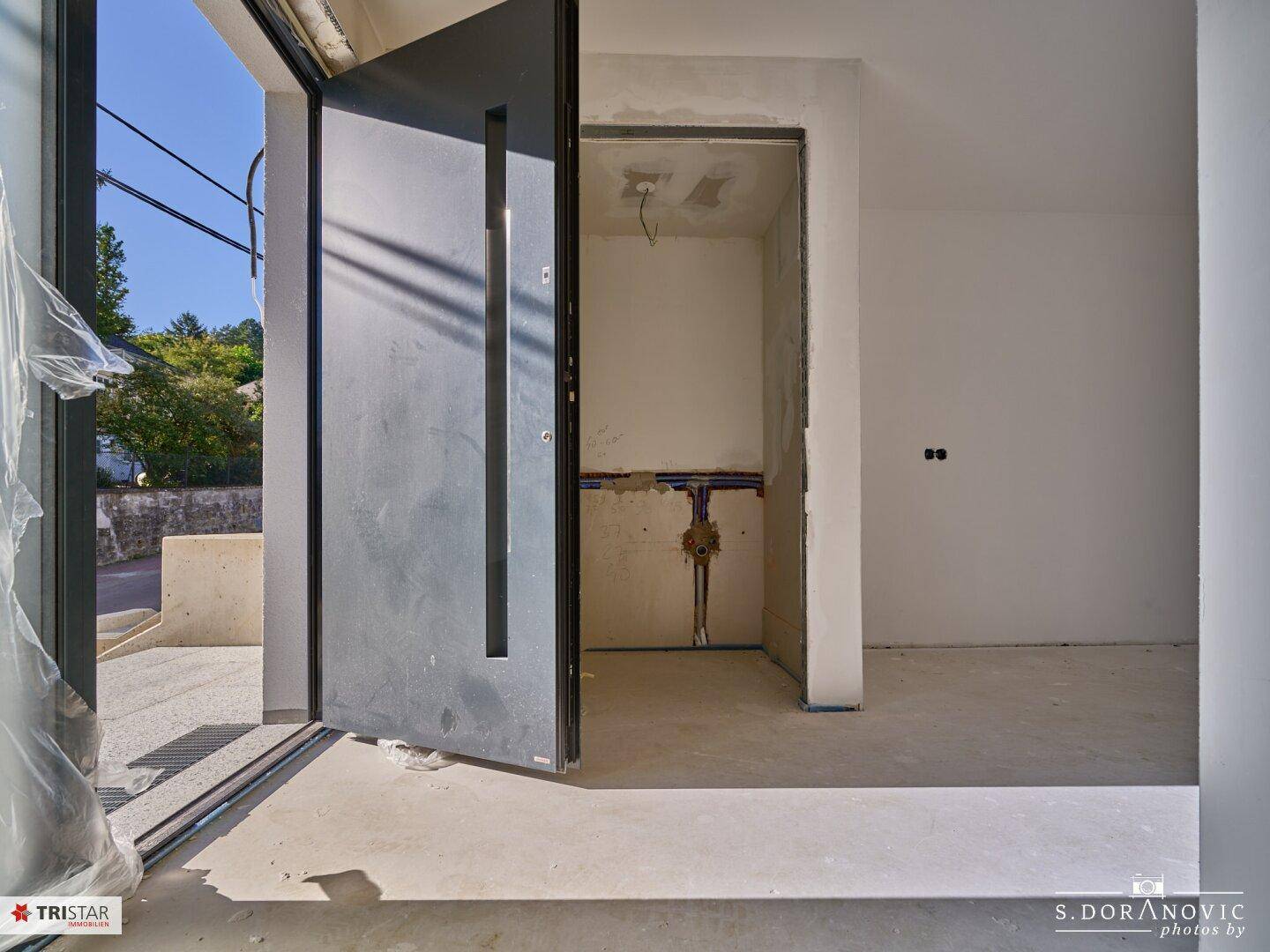Eingangsbereich mit moderner Haustür und Zugang zu einem kleinen Abstellraum.