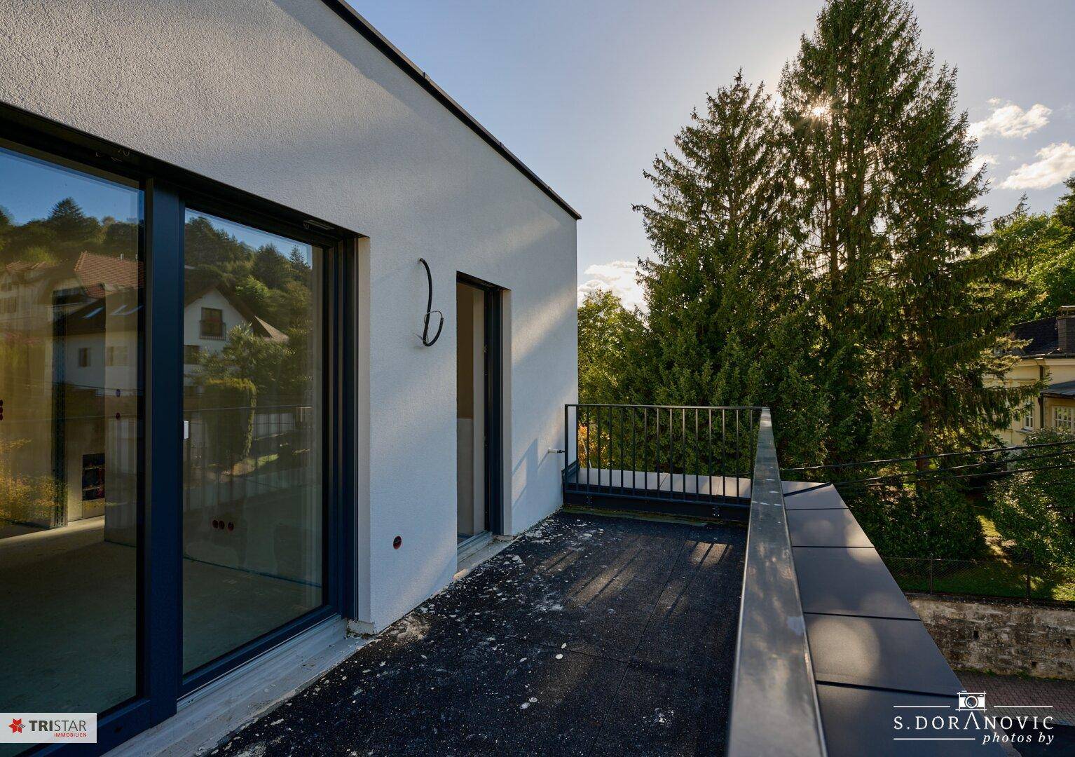 Sonniger Terrassenbereich mit großen Schiebetüren und Blick auf die grüne Umgebung.