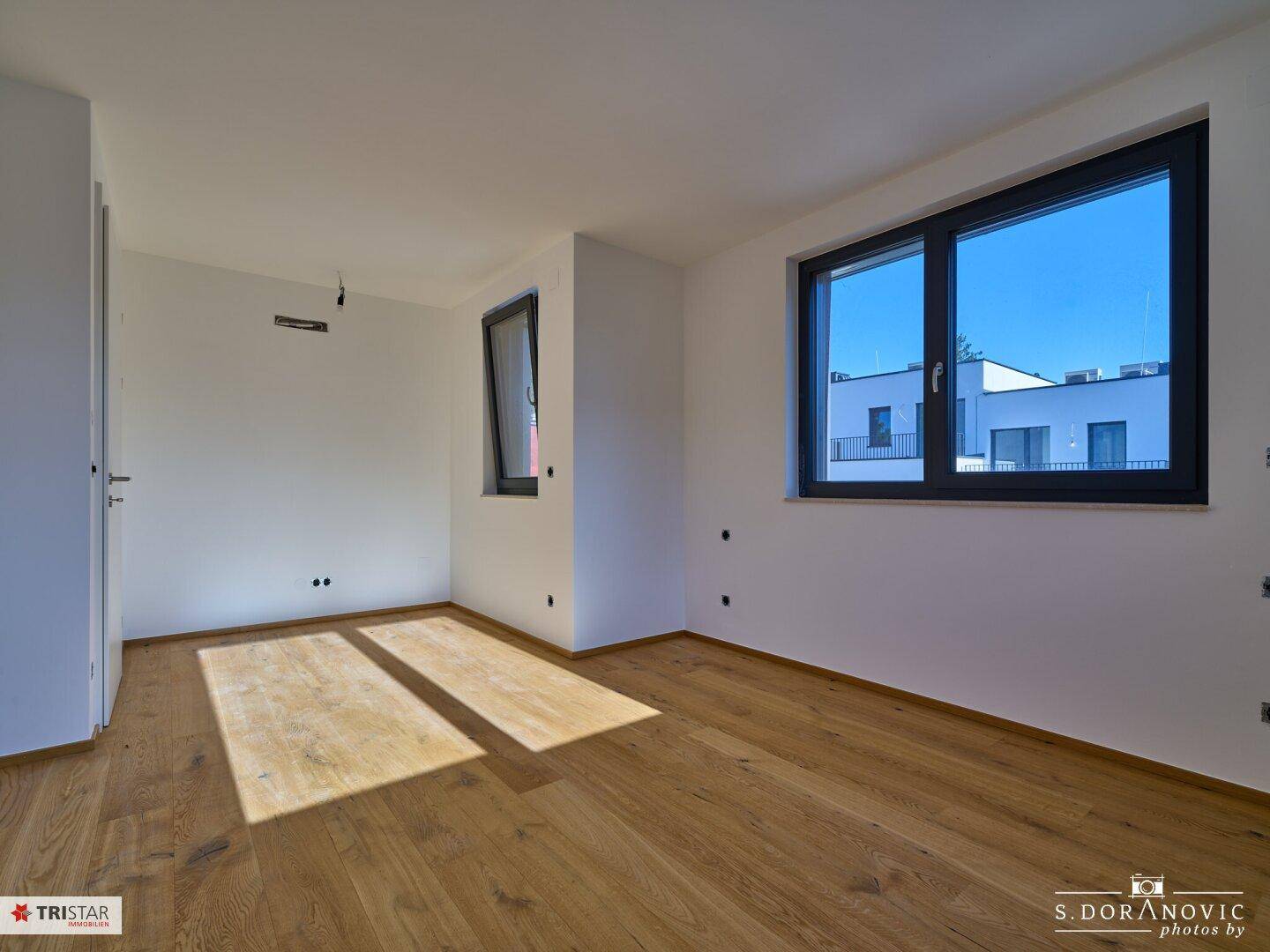 Helles Schlafzimmer mit Holzboden und mehreren Fenstern, die einen weiten Blick bieten.