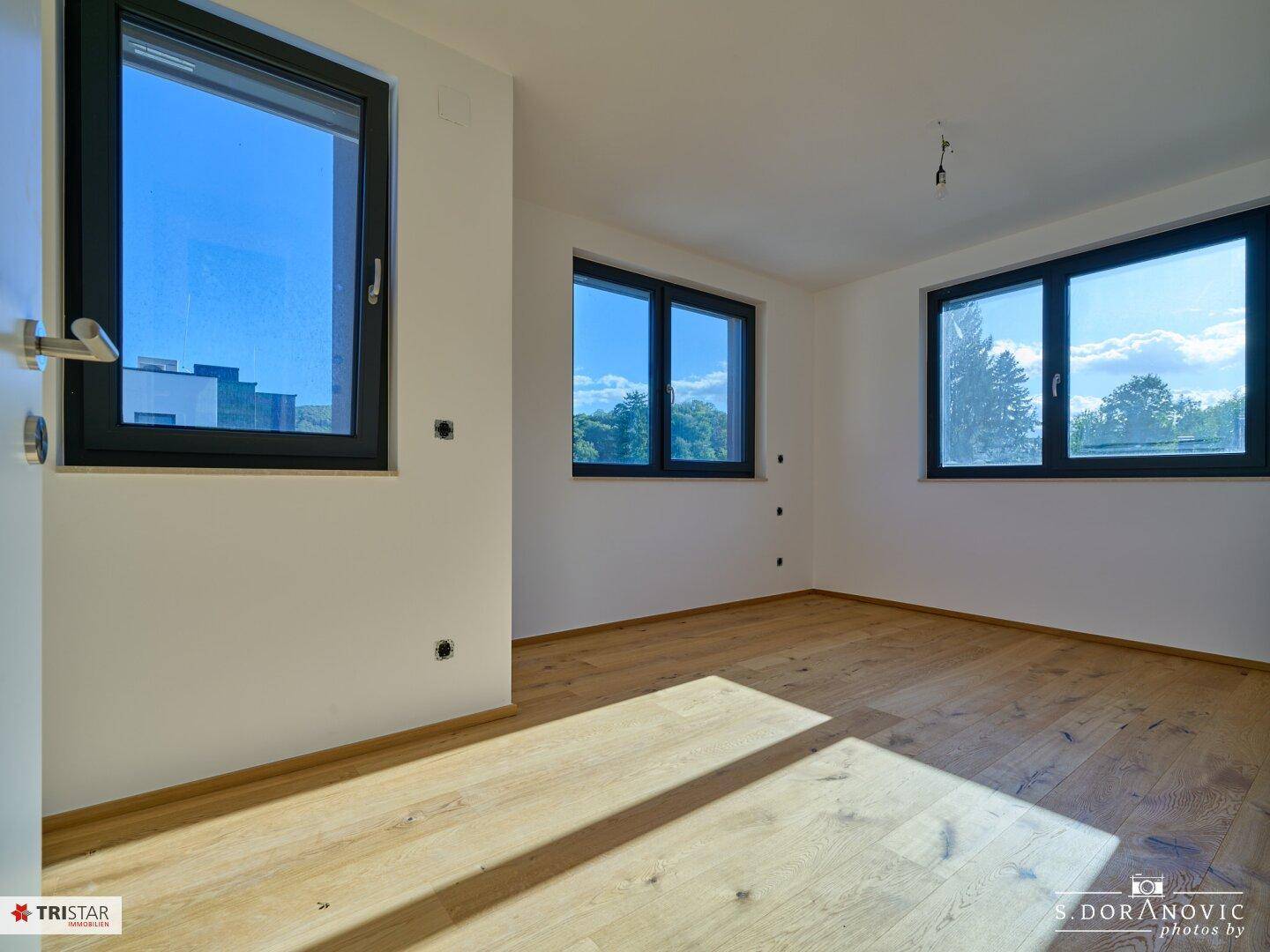Lichtdurchflutetes Schlafzimmer mit neuem Hartholzboden und mehreren Fenstern mit Blick ins Grüne.