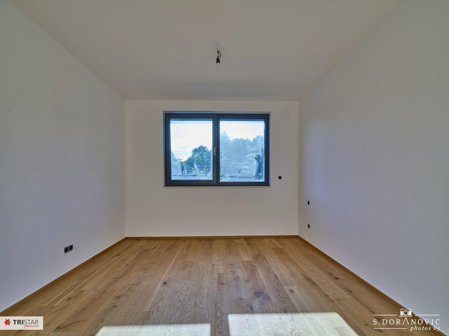Sonniger Raum mit neuem Hartholzboden und einem Fenster, das einen weiten Blick in die Natur ermöglicht.
