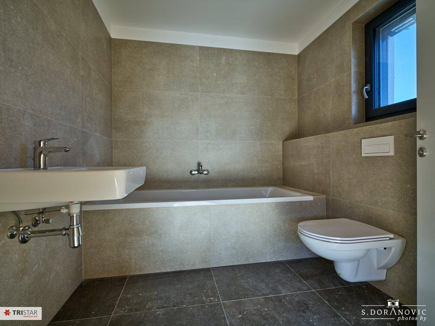 Modernes Badezimmer mit Badewanne, Waschbecken, wandhängendem WC und Fenster.