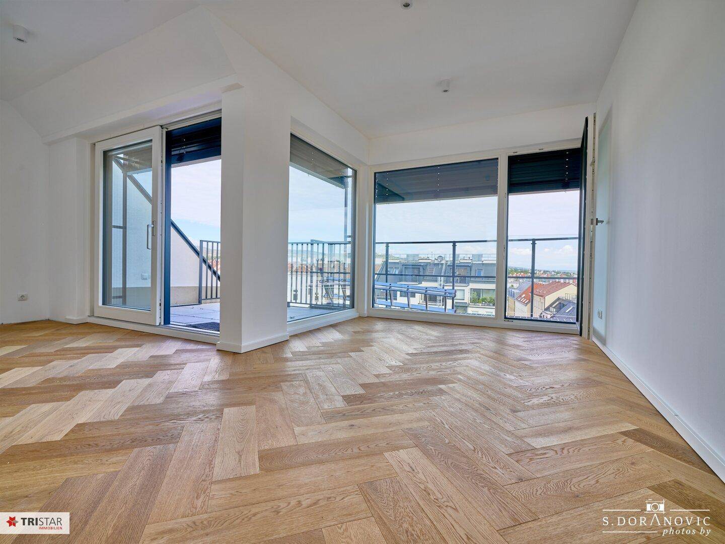 Geräumiges Wohnzimmer mit Fischgrätparkett und Zugang zu einem großen Balkon mit Stadtblick.