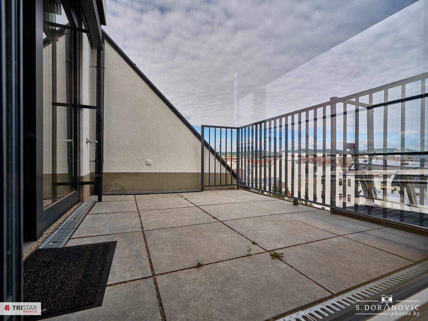 Weitläufige Dachterrasse mit Fliesen und Glasgeländer, ideal für Entspannung im Freien.