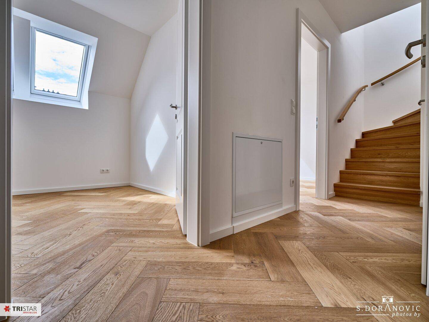 Flur mit Fischgrätparkett, Zugang zu einem Zimmer und Treppe zum oberen Stockwerk.