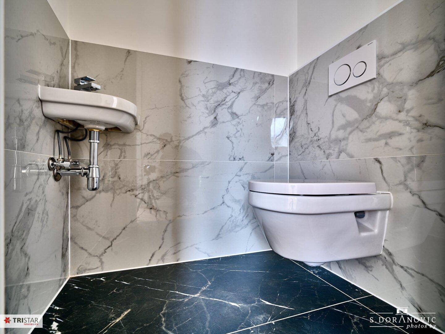Modernes Gäste-WC mit Marmorfliesen an Wänden und dunklem Boden, wandhängendes WC.
