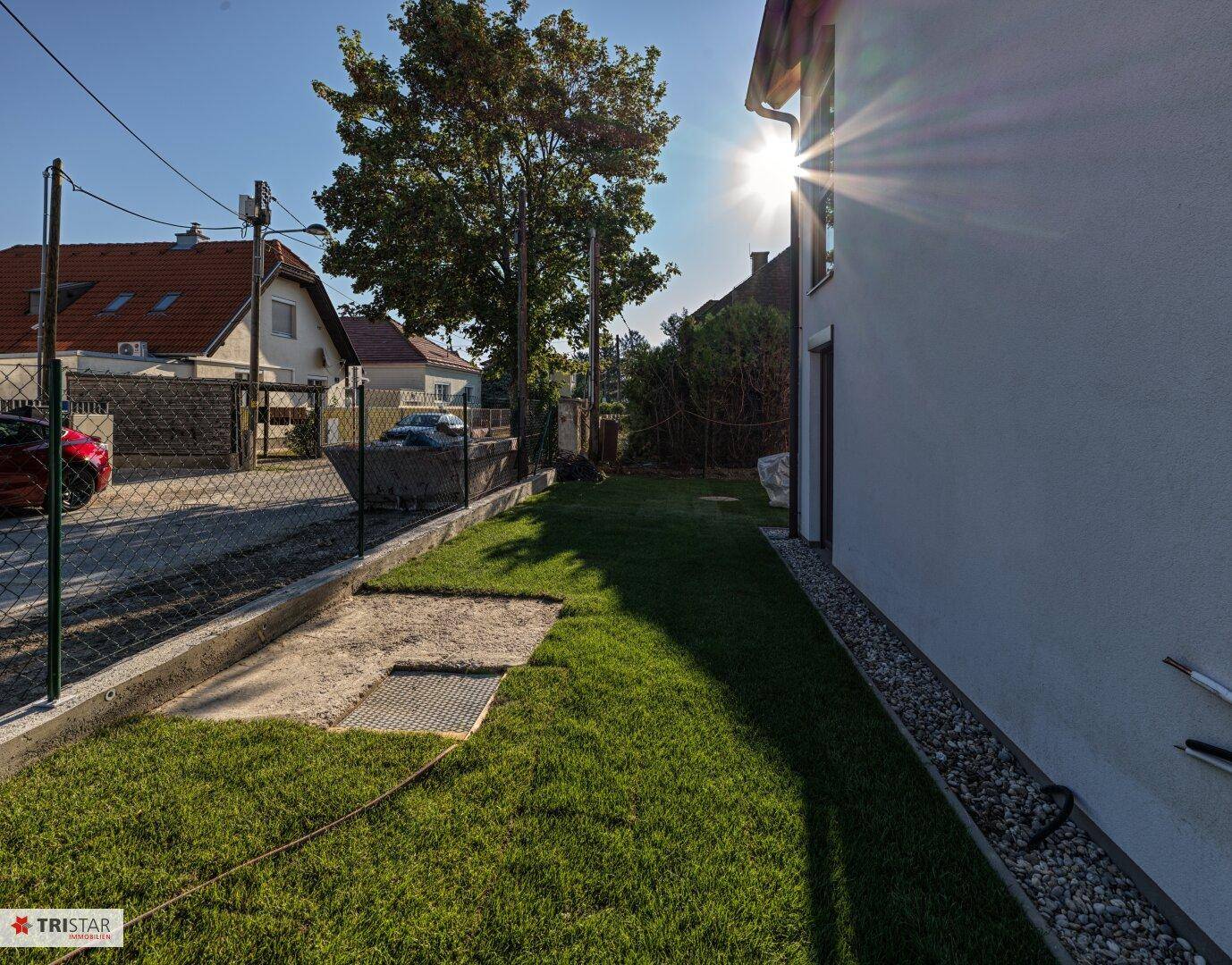 Seitlicher Gartenbereich mit Rasenfläche und Kiesstreifen entlang der Hauswand bei Sonnenschein.