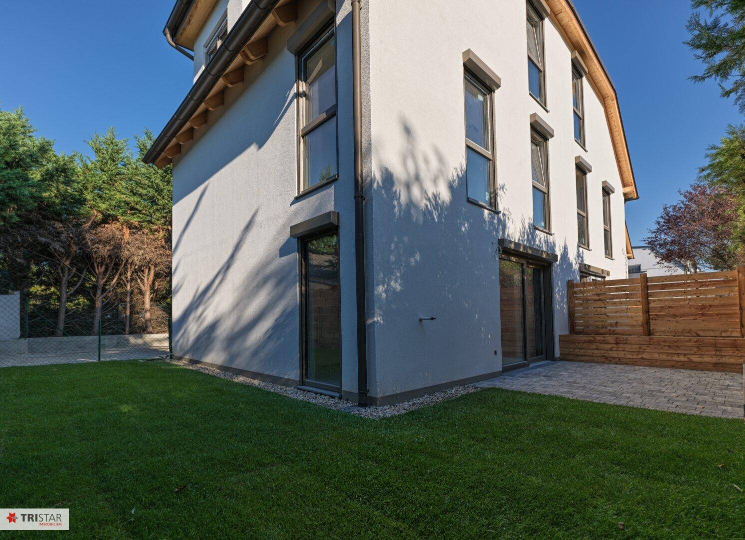 Seitenansicht des modernen Hauses mit Rasenfläche und gepflastertem Bereich an einem sonnigen Tag.