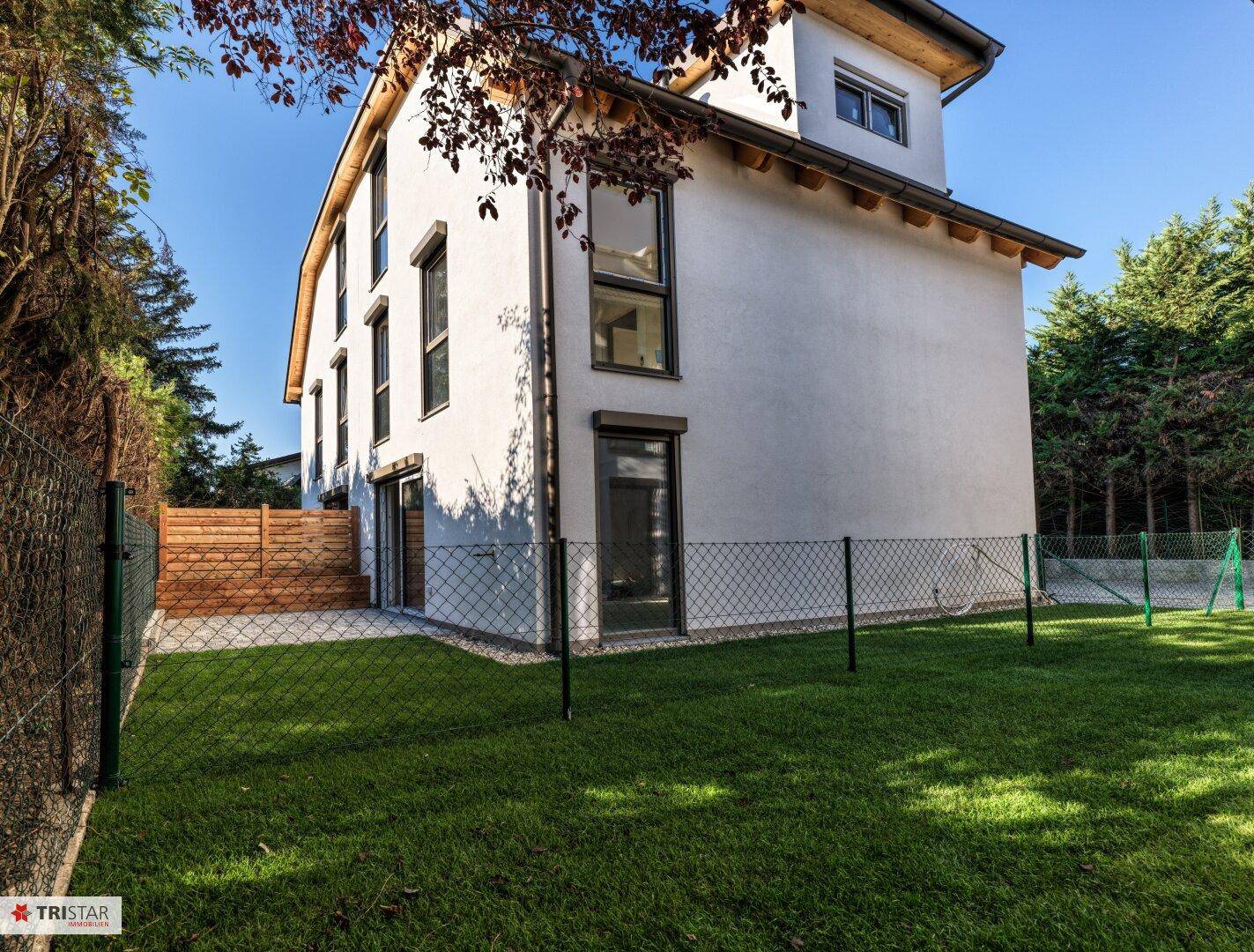 Weitläufiger Gartenbereich mit grünem Rasen und umgebenden Bäumen neben dem Neubau.