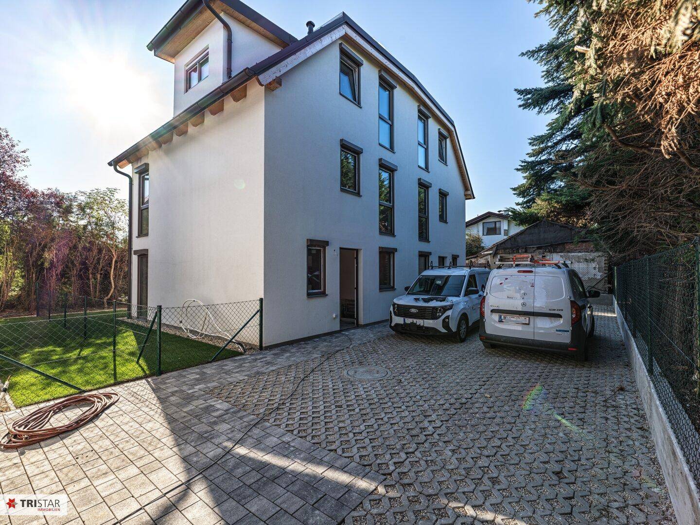 Seitenansicht eines modernen Hauses mit gepflasterter Einfahrt und Parkmöglichkeiten.