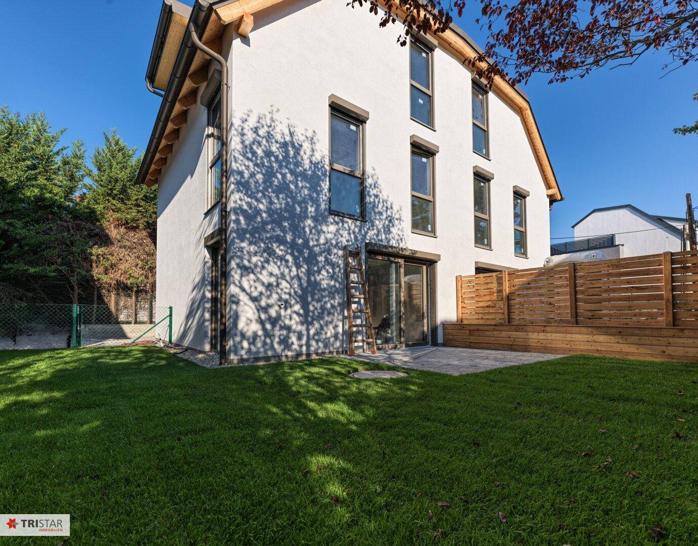 Weißes Einfamilienhaus mit Terrasse, Rasenfläche und neuem Holzzaun im sonnigen Garten.