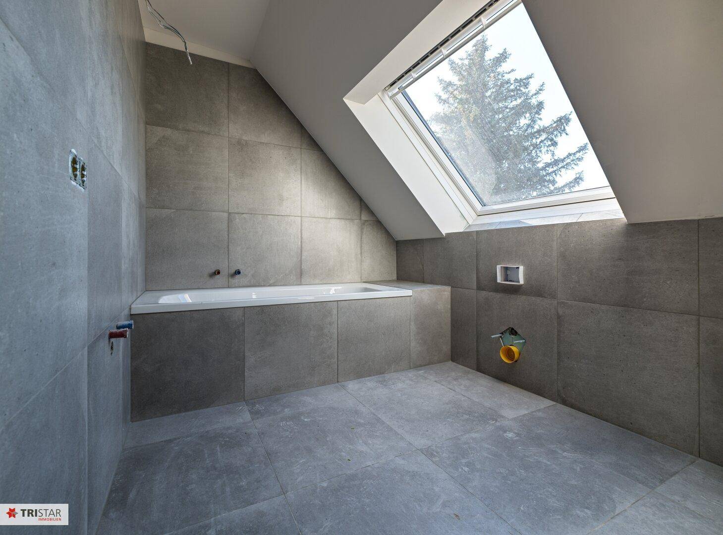 Modernes Badezimmer im Dachgeschoss mit grauen Fliesen, Badewanne und großem Dachfenster.