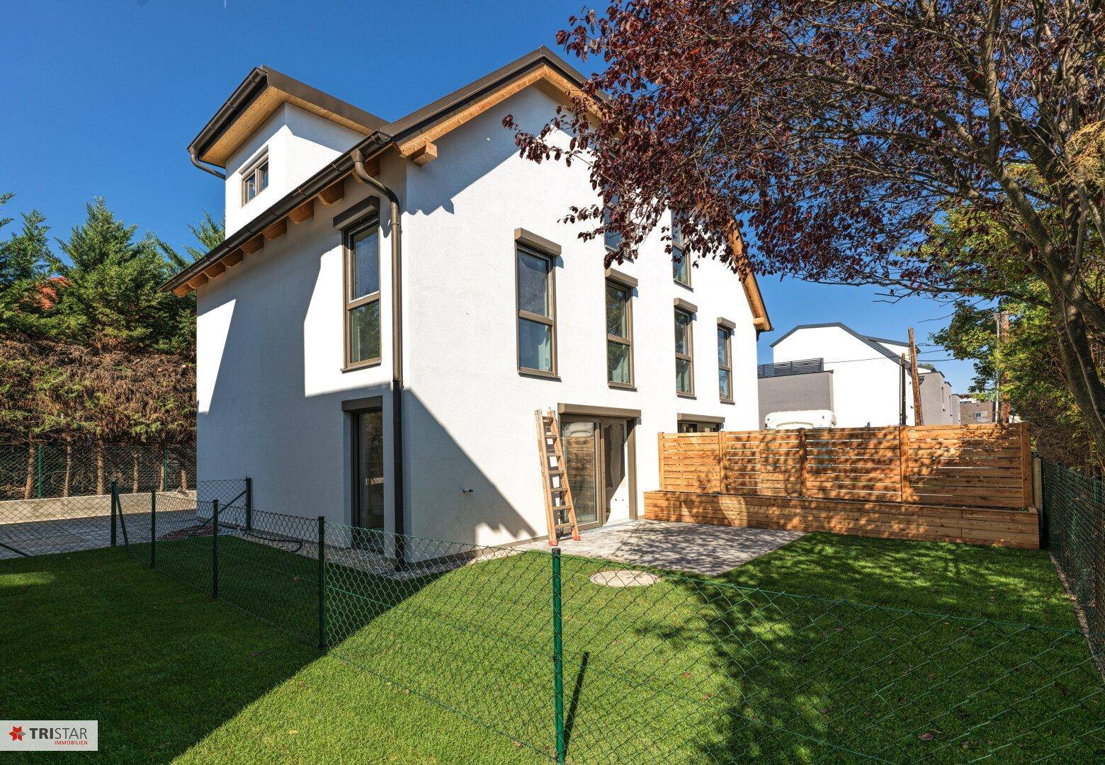 Weißes Einfamilienhaus mit Terrasse, Rasenfläche und neuem Holzzaun im sonnigen Garten.