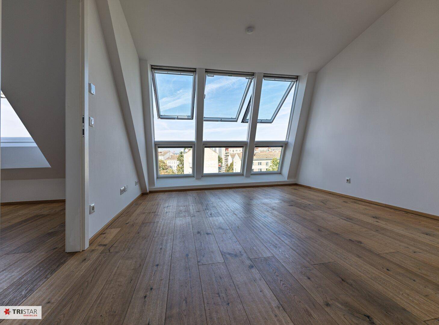 Lichtdurchfluteter Wohnbereich im Dachgeschoss mit Holzboden und weitem Blick über die Stadt.