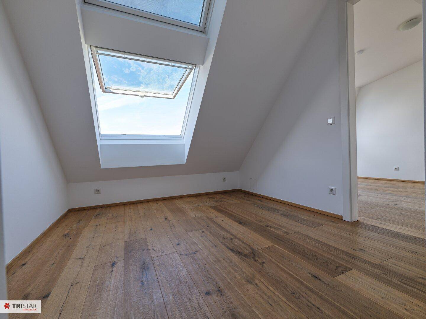 Gemütliches Zimmer im Dachgeschoss mit Holzboden und einem großen Dachfenster für viel Helligkeit.