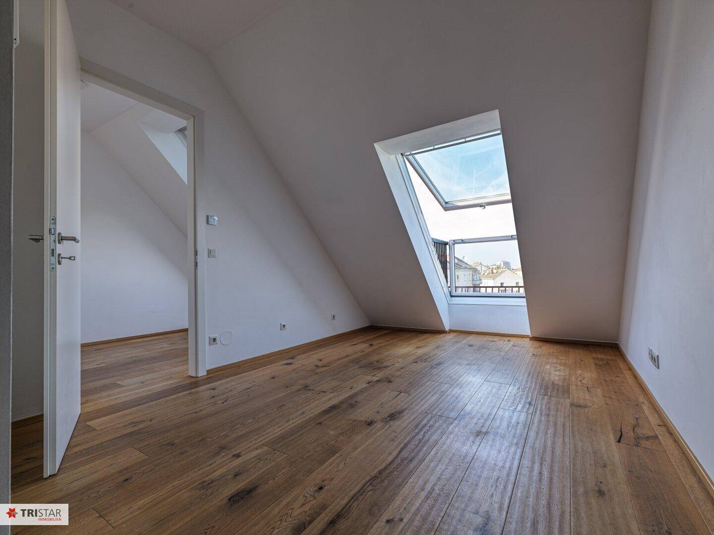 Heller Raum im Dachgeschoss mit Holzboden und großem Dachfenster, das viel Licht spendet.