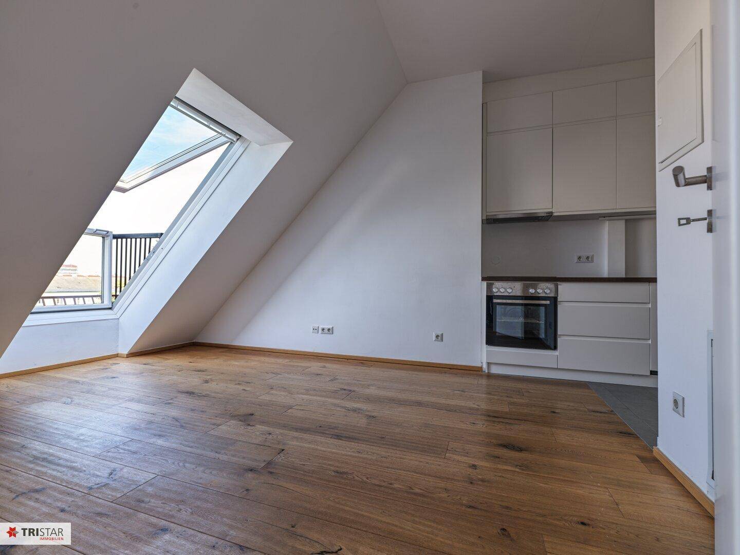 Offener Wohnbereich im Dachgeschoss mit integrierter Küche, Holzboden und Dachfenster.