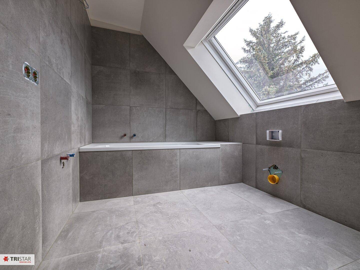 Modernes Badezimmer im Bau mit grauen Fliesen, eingebauter Badewanne und großem Dachfenster für viel Licht.