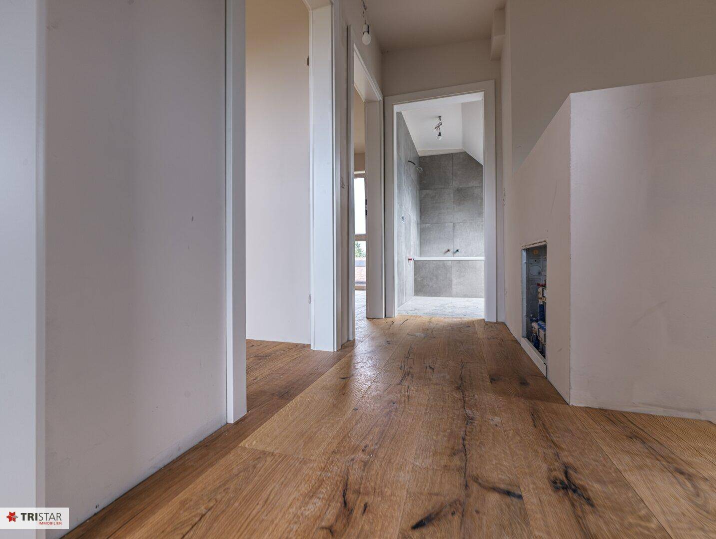 Heller Flur mit Holzdielenboden und Blick in ein Badezimmer im Rohbauzustand.