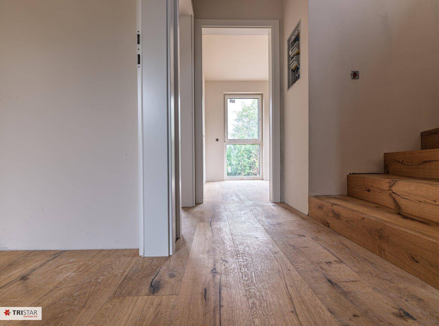 Heller Flur mit Holzdielenboden und Blick auf eine Tür, die ins Freie führt.