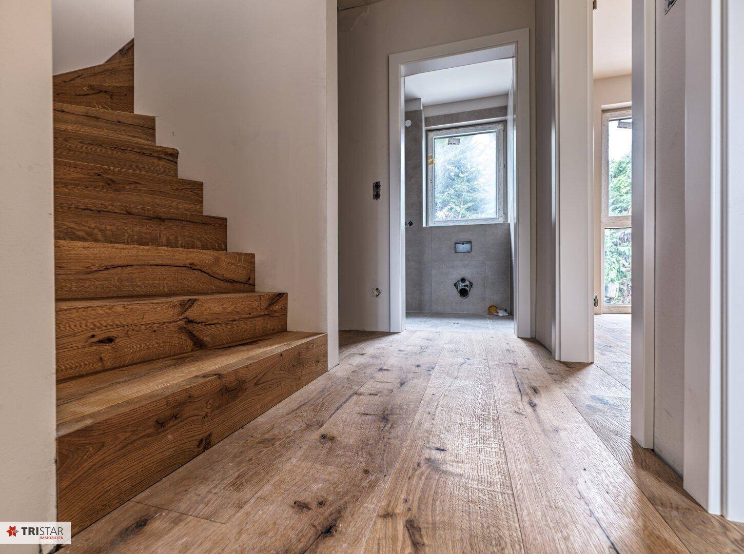 Heller Flur mit Holztreppe und passendem Holzfußboden, der zu verschiedenen Räumen führt.