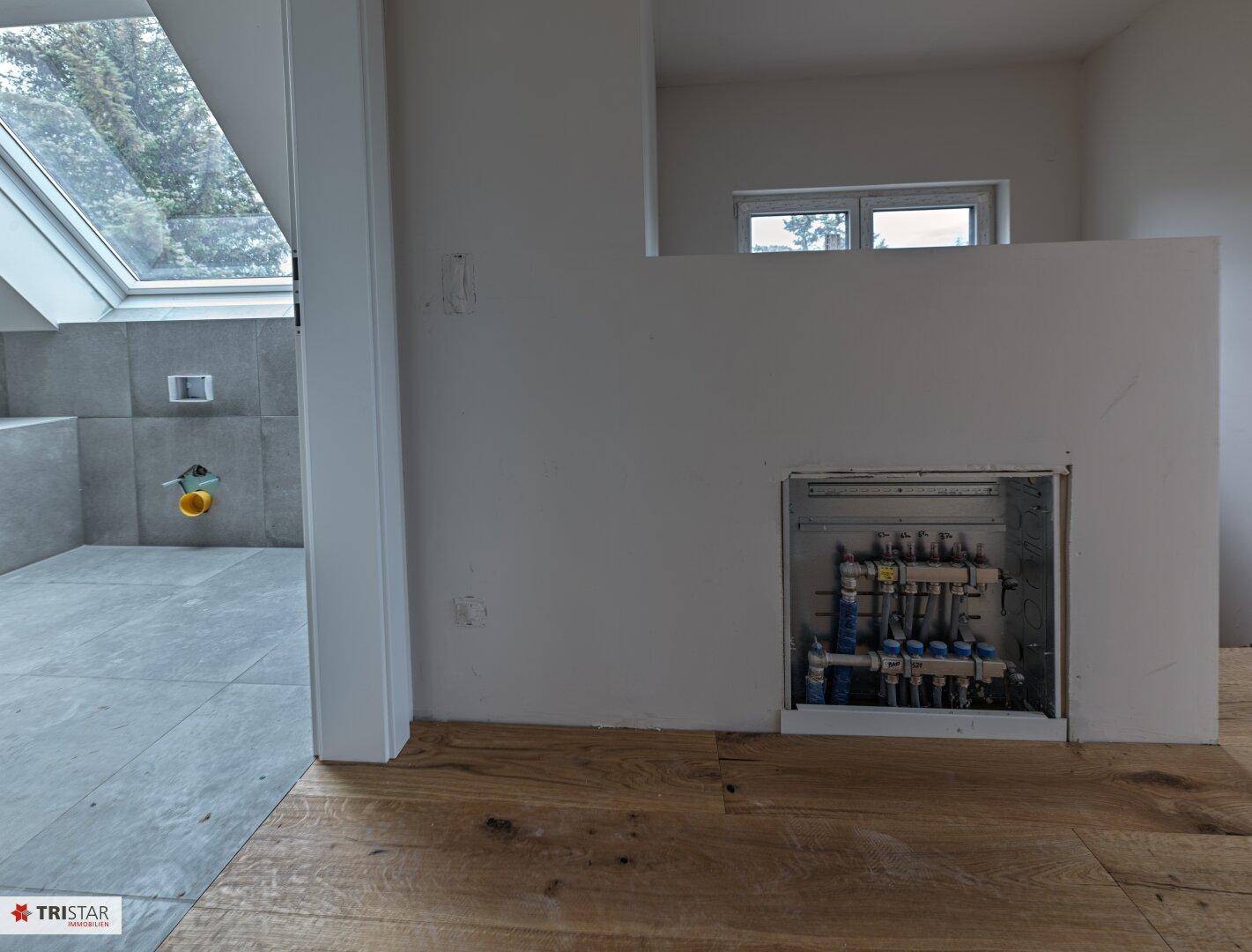 Innenansicht eines Flurs mit Holzboden und Blick auf ein Badezimmer mit Dachfenster.