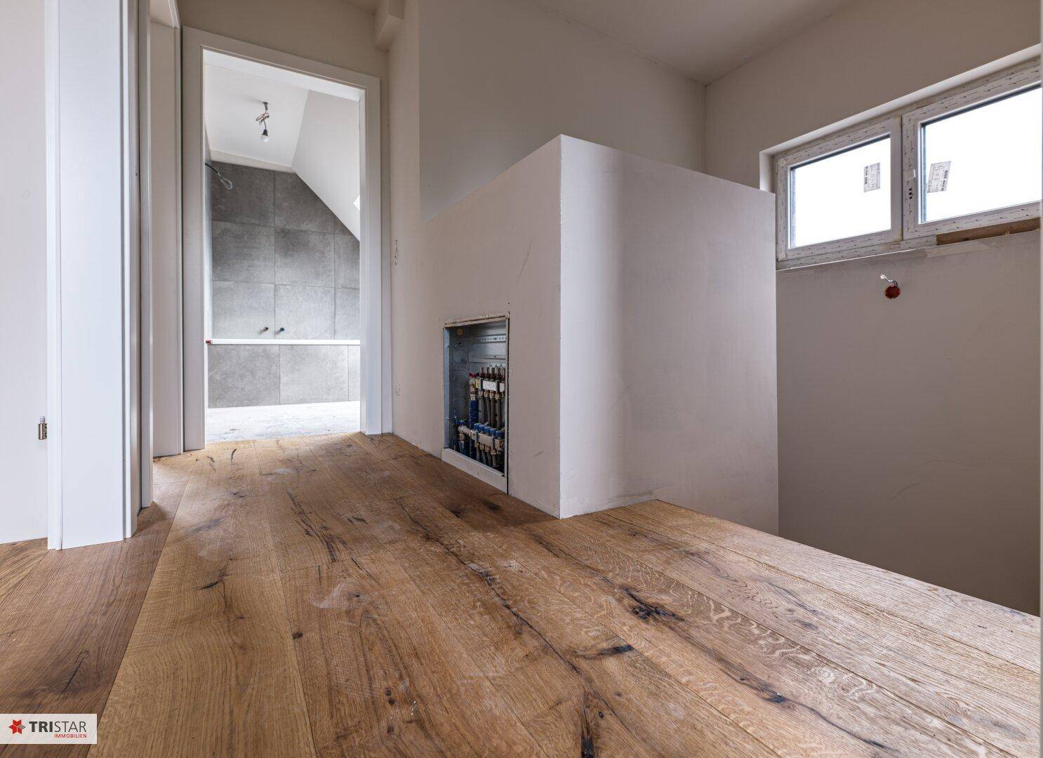 Heller Flur mit neu verlegtem Holzboden und Blick in ein Badezimmer im Bau.