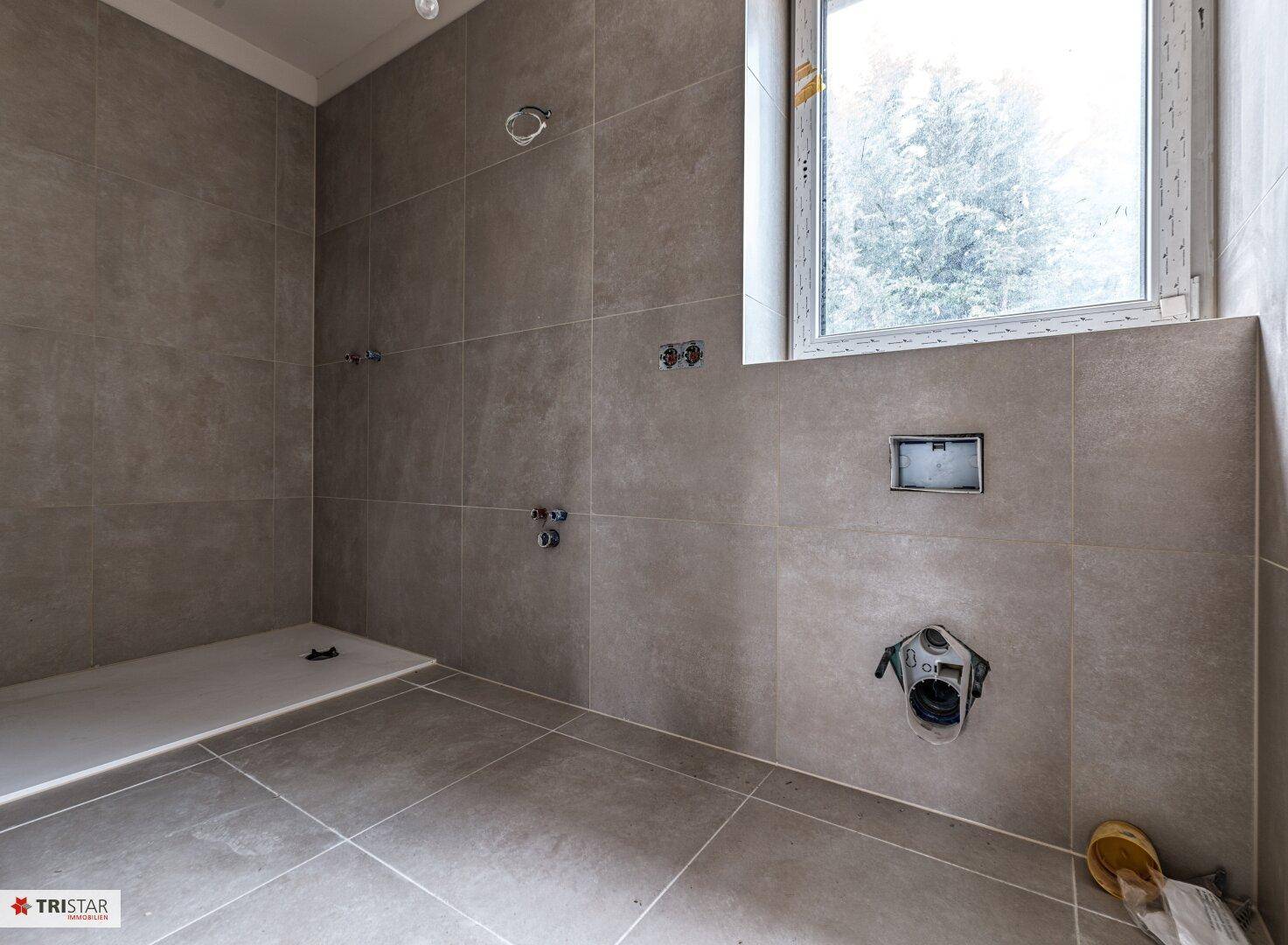 Modernes Badezimmer im Rohbau mit großen Fliesen und vorbereiteter Duschfläche.