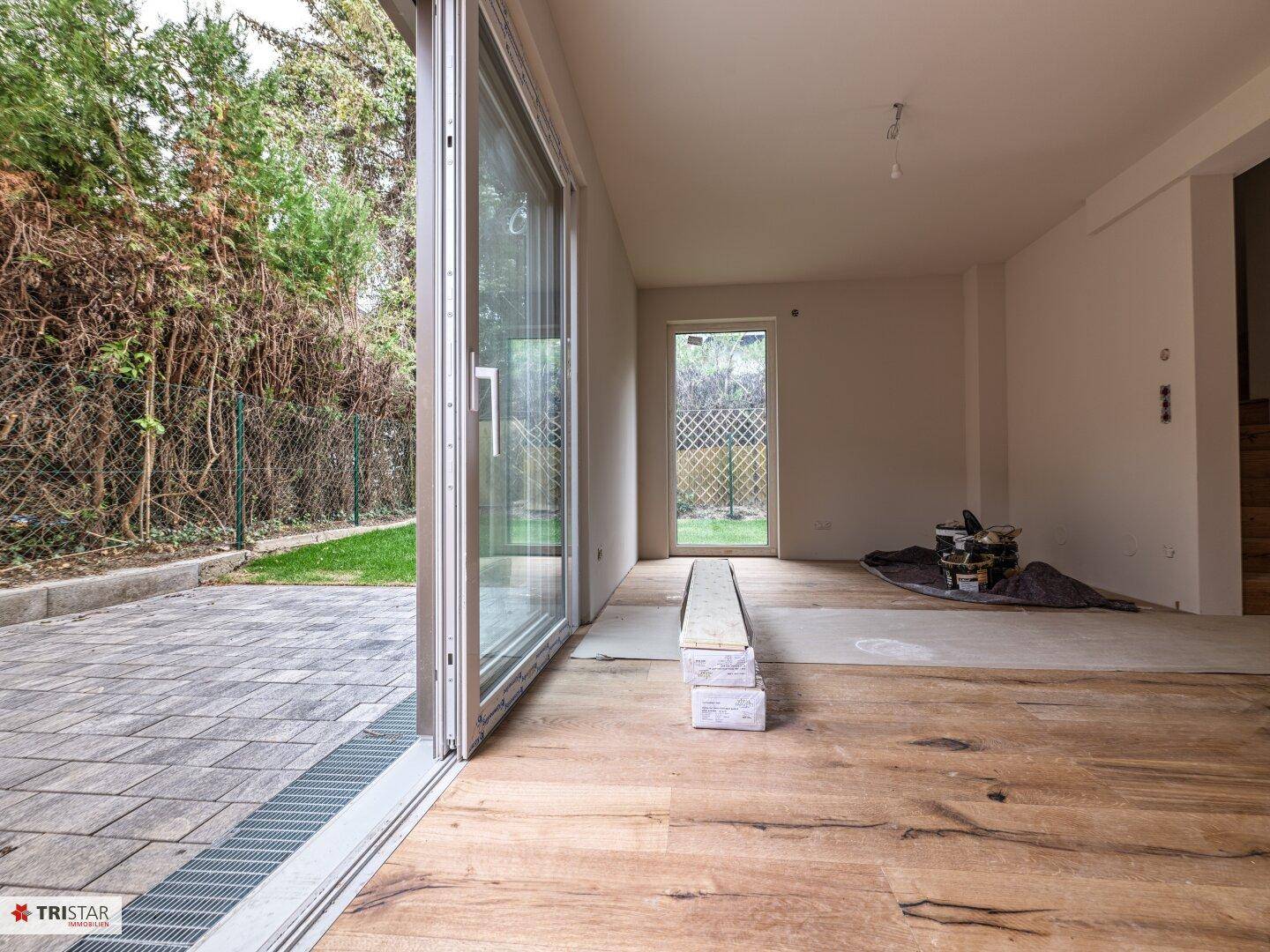 Geräumiger, unmöblierter Wohnbereich mit Holzdielenboden und Zugang zur Terrasse und Garten.