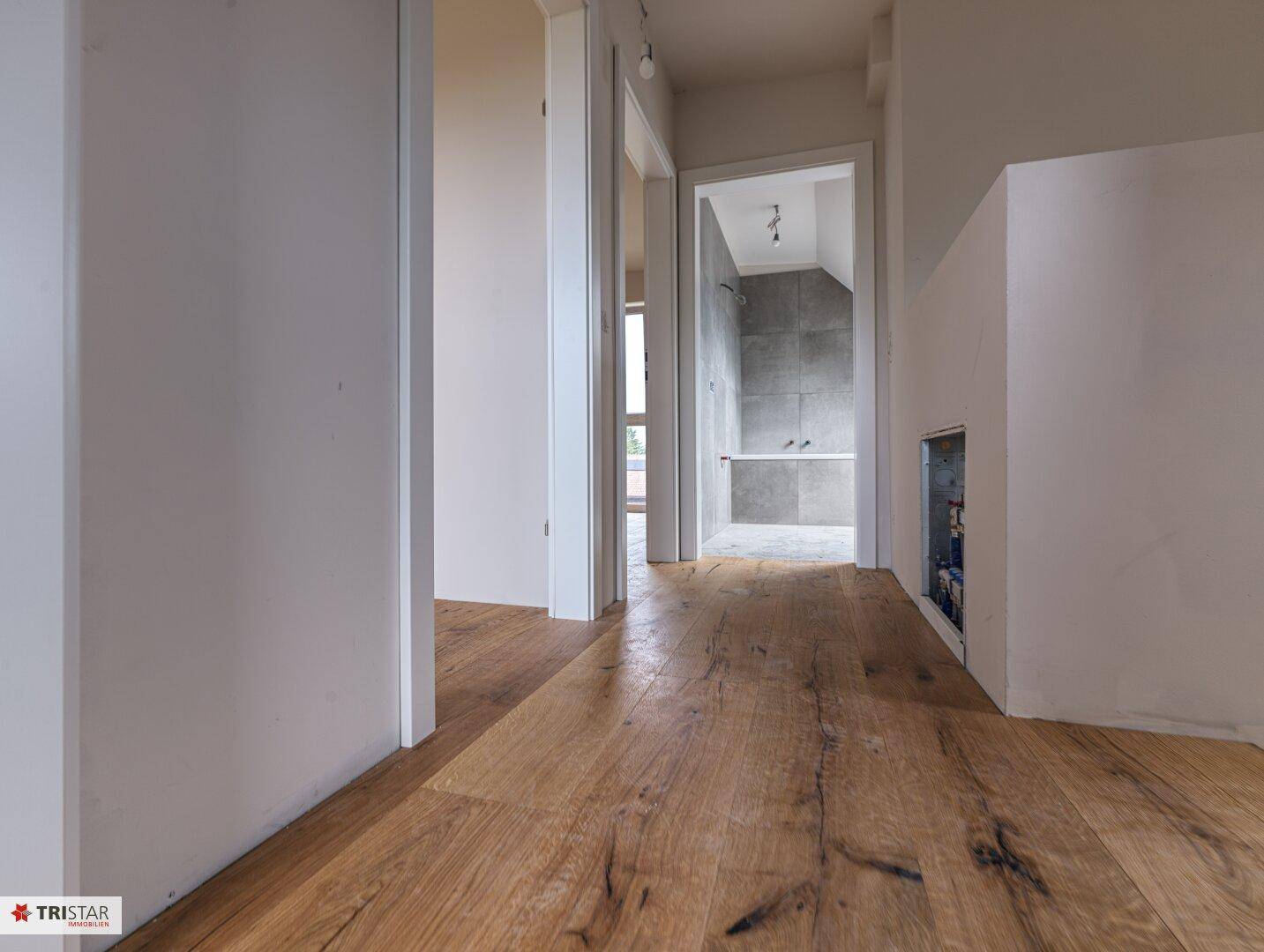 Flur mit Holzdielenboden und Blick in ein Badezimmer im Dachgeschoss.