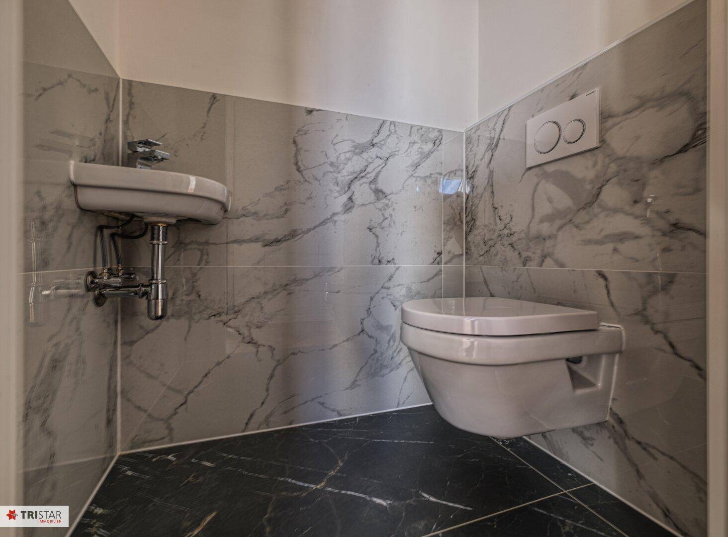 Modernes Gäste-WC mit Marmoroptik-Fliesen, wandhängendem WC und kleinem Waschbecken.