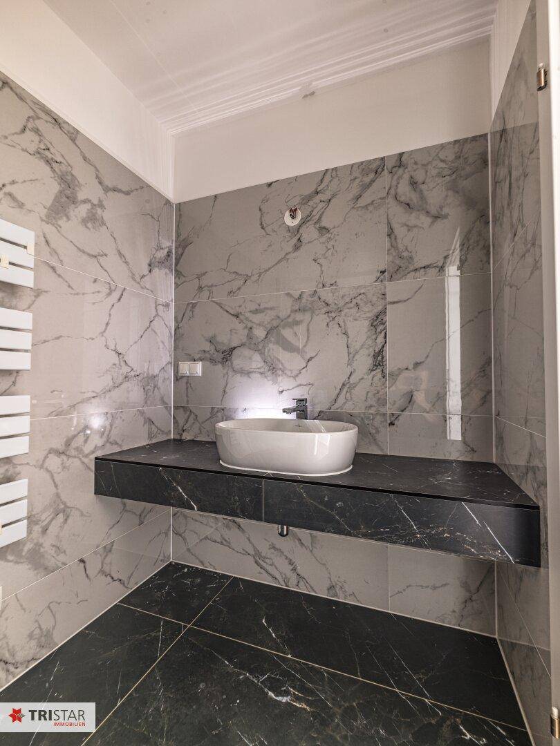 Elegantes Badezimmer mit Marmorfliesen, dunklem Boden, schwebendem Waschtisch und beheiztem Handtuchhalter.