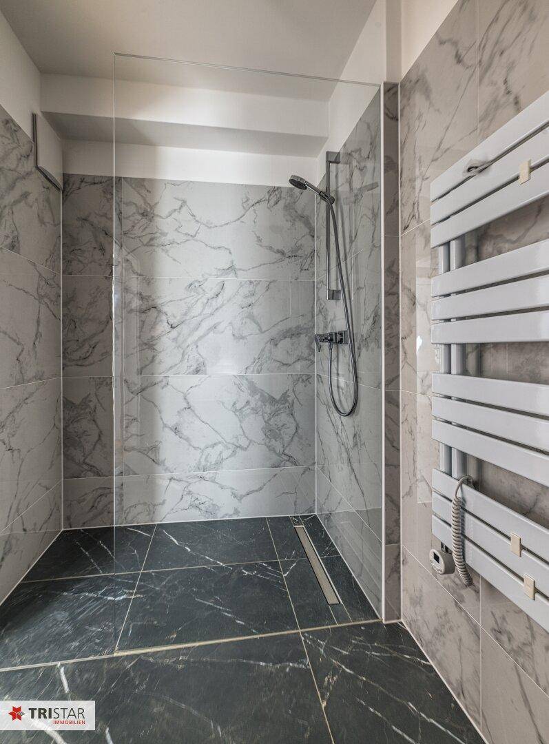 Geräumige begehbare Dusche in einem modernen Badezimmer mit Marmorfliesen und Handtuchheizkörper.
