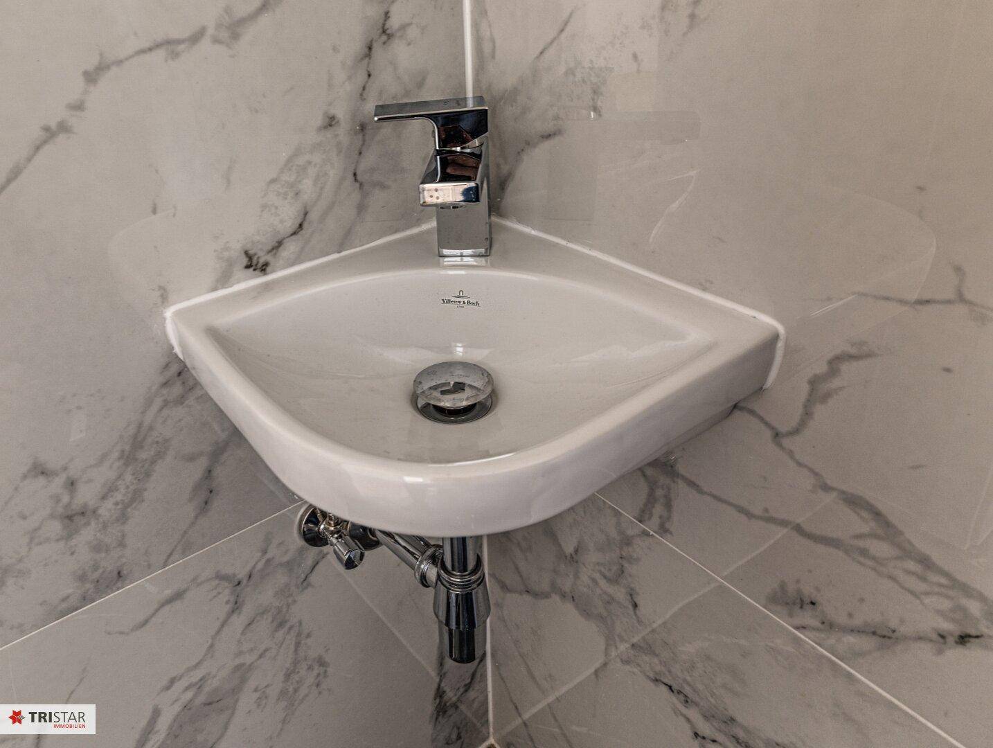 Nahaufnahme eines modernen Eckwaschbeckens mit Chromarmatur in einem stilvollen Gäste-WC.