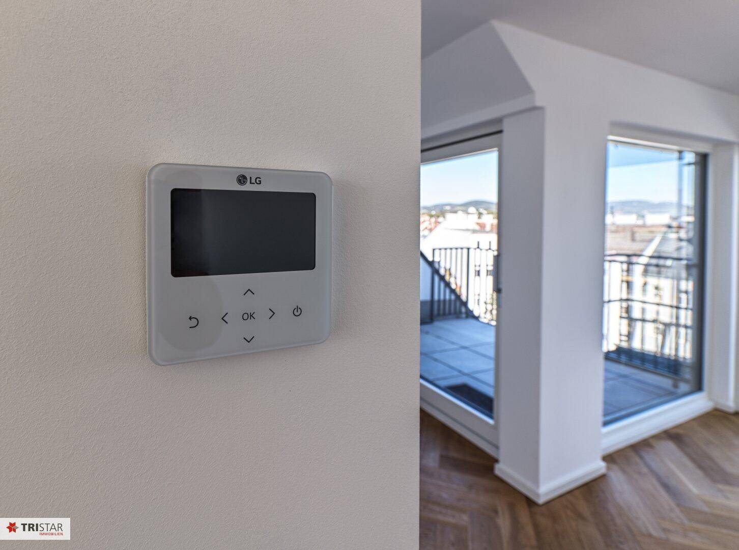 Modernes LG-Thermostat an der Wand mit Blick auf einen Balkon und die Stadt im Hintergrund.