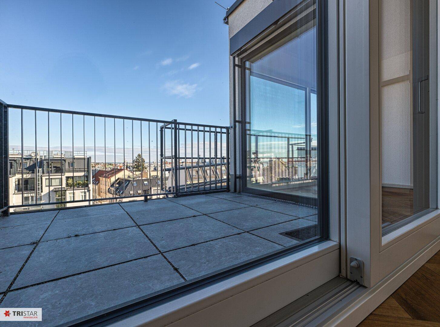 Große Terrasse mit grauen Fliesen, schwarzem Geländer und Panoramablick über die Stadt.