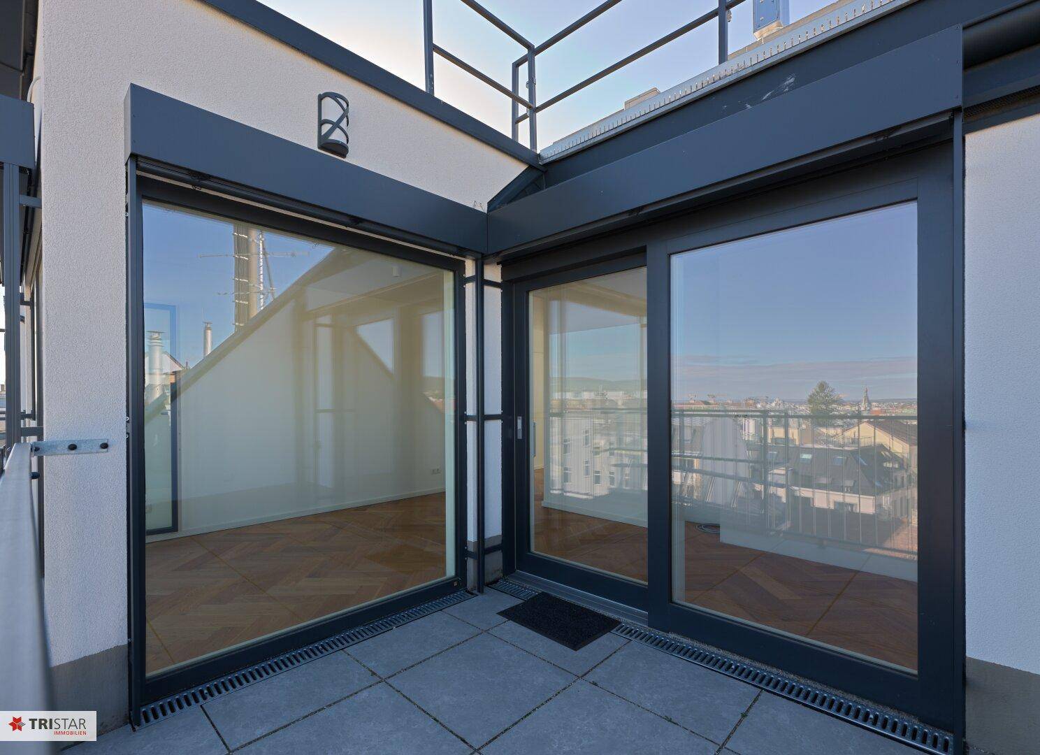 Moderne Terrasse mit grauen Fliesen und großen Glasfronten, die einen weiten Stadtblick bieten.