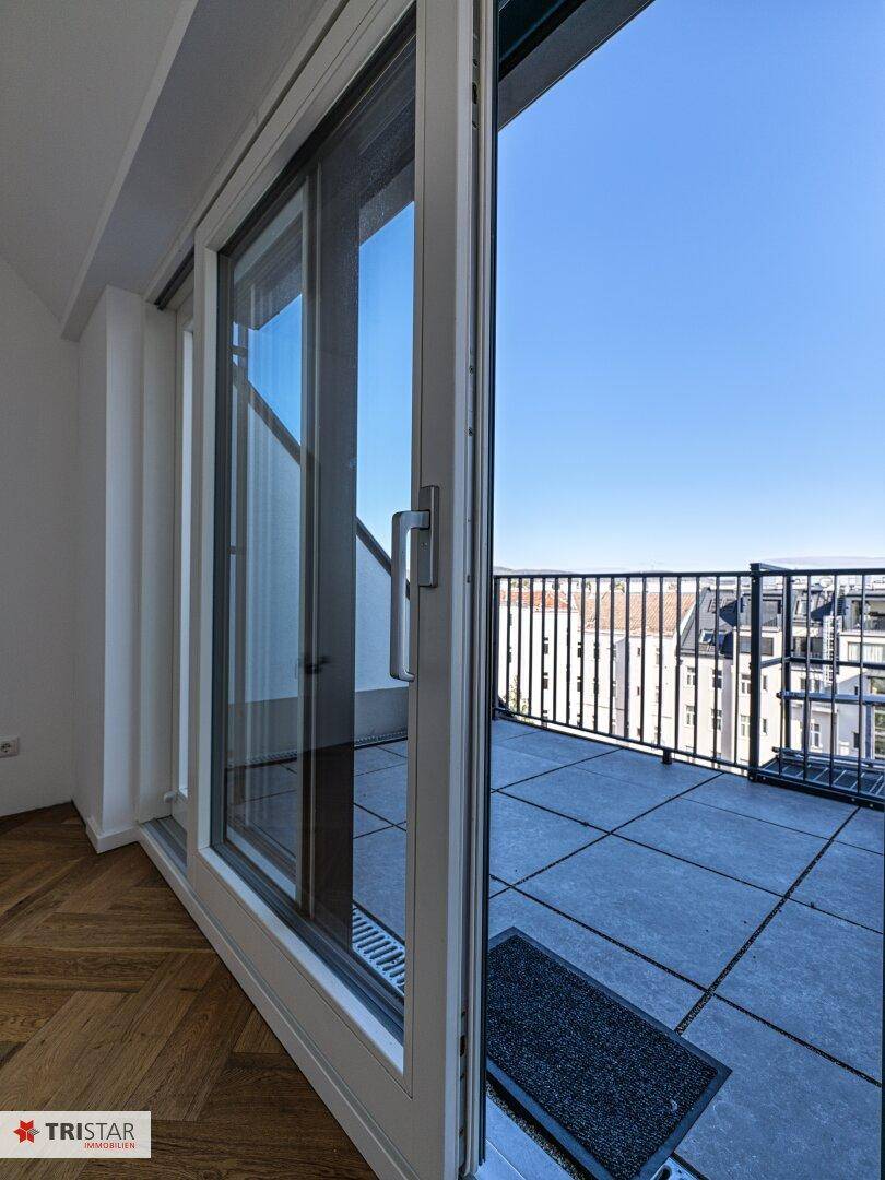 Offene Schiebetür führt auf eine geflieste Terrasse mit schwarzem Geländer und Stadtblick.