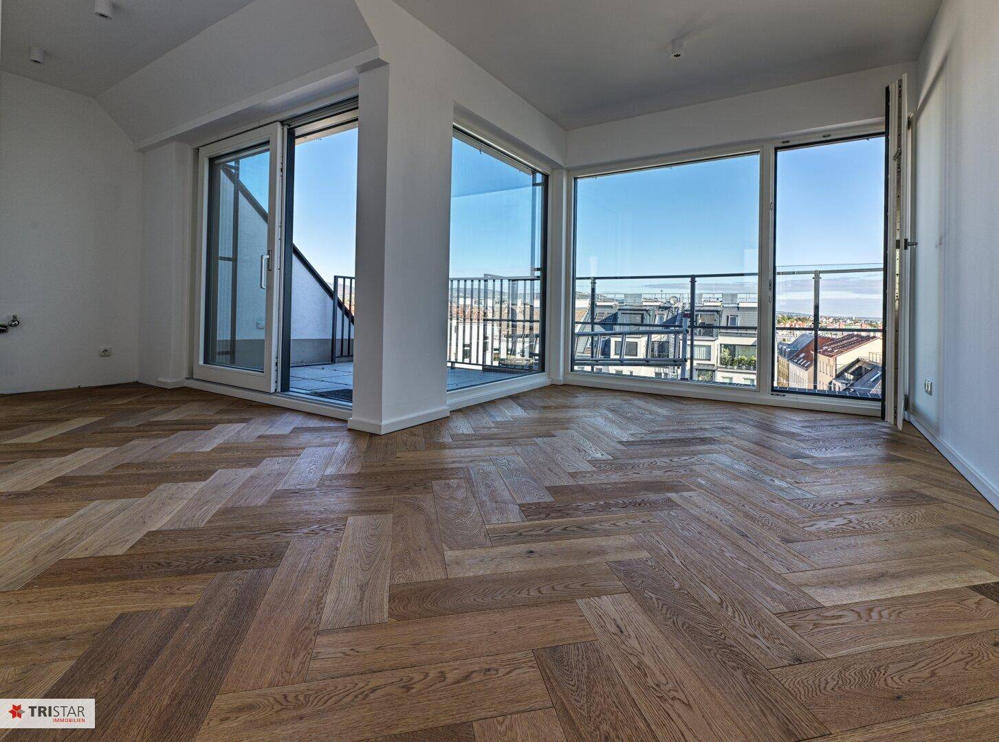 Geräumiger Wohnbereich mit Fischgrätparkett, großen Fenstern und Zugang zu einem Balkon mit Stadtblick.