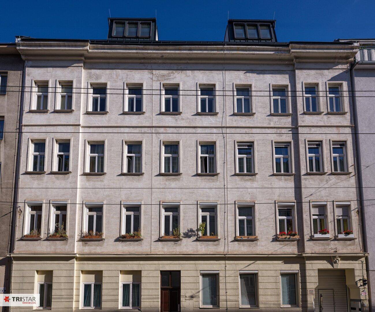 Klassische Fassade eines Altbaus mit vielen Fenstern und Dachgauben unter blauem Himmel.