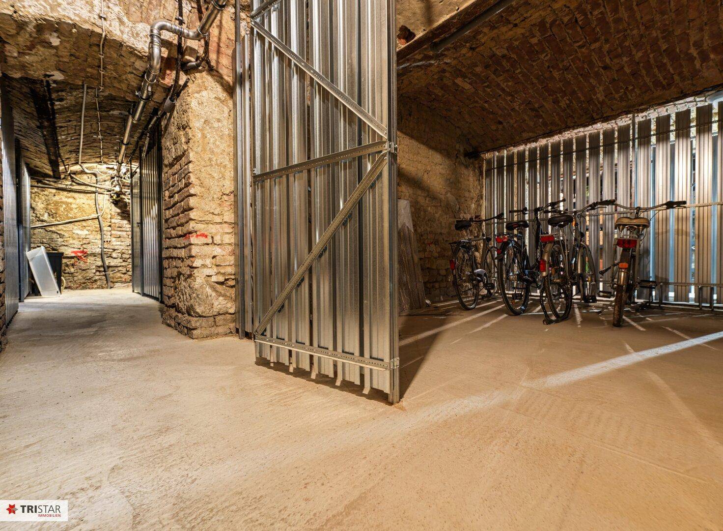 Geräumiger Fahrradraum im Keller mit robusten Metallabtrennungen und unverputzten Ziegelwänden.