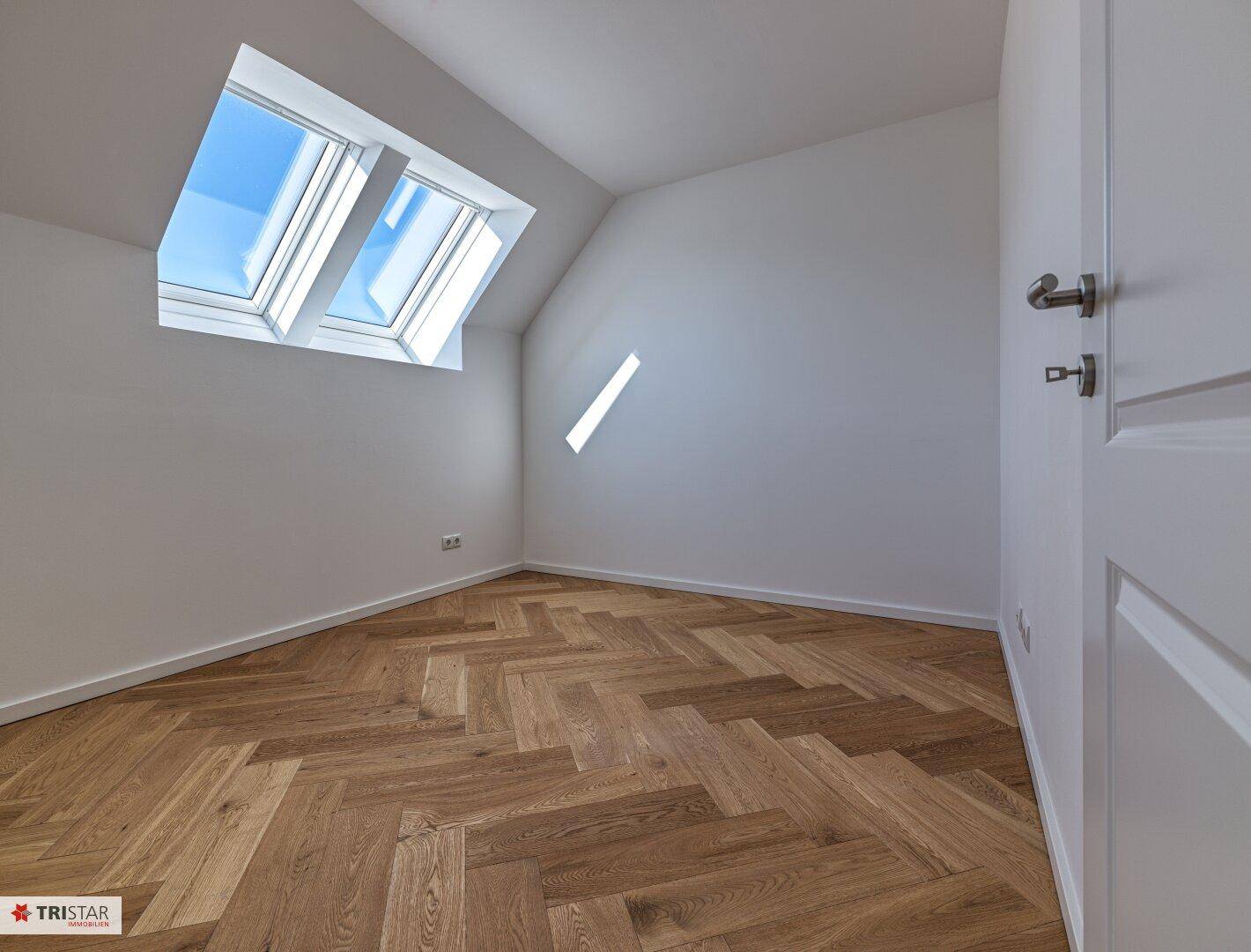 Helles Zimmer mit Dachschräge, Fischgrätparkett und einem Dachfenster für natürliches Licht.