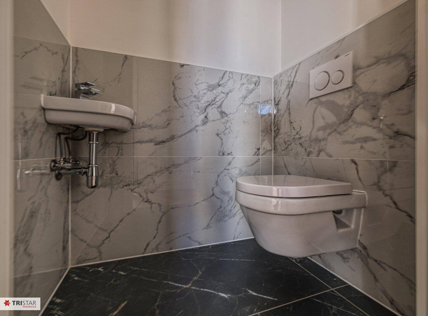 Modernes Gäste-WC mit eleganten Marmorfliesen, wandhängendem WC und kleinem Waschbecken.