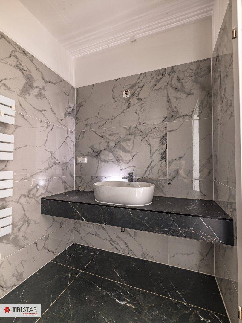 Modernes Badezimmer mit Marmorfliesen, schwebendem Waschtisch und ovalem Aufsatzwaschbecken.
