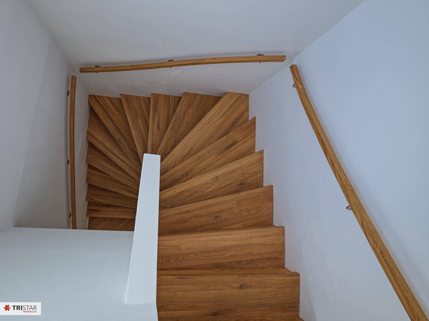 Elegante Holztreppe mit geschwungenem Geländer, die die verschiedenen Ebenen verbindet.
