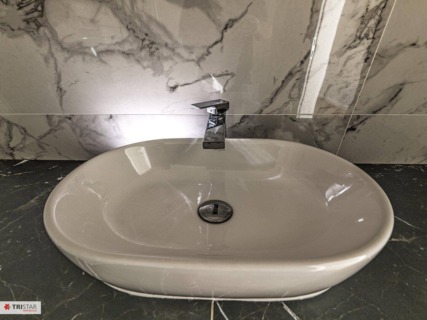 Nahaufnahme eines modernen Aufsatzwaschbeckens auf einer dunklen Marmorplatte im Badezimmer.