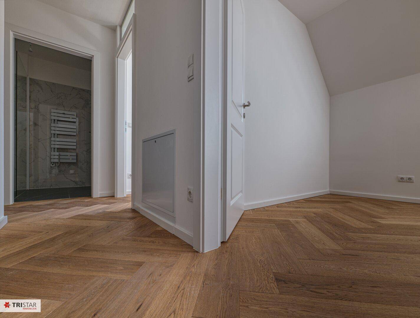 Heller Flur mit Fischgrätparkett und Zugang zu einem modernen Badezimmer.