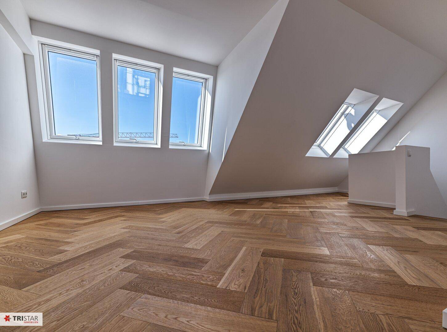 Geräumiges Zimmer mit Dachschrägen, Fischgrätparkett und zwei Dachfenstern für viel Tageslicht.